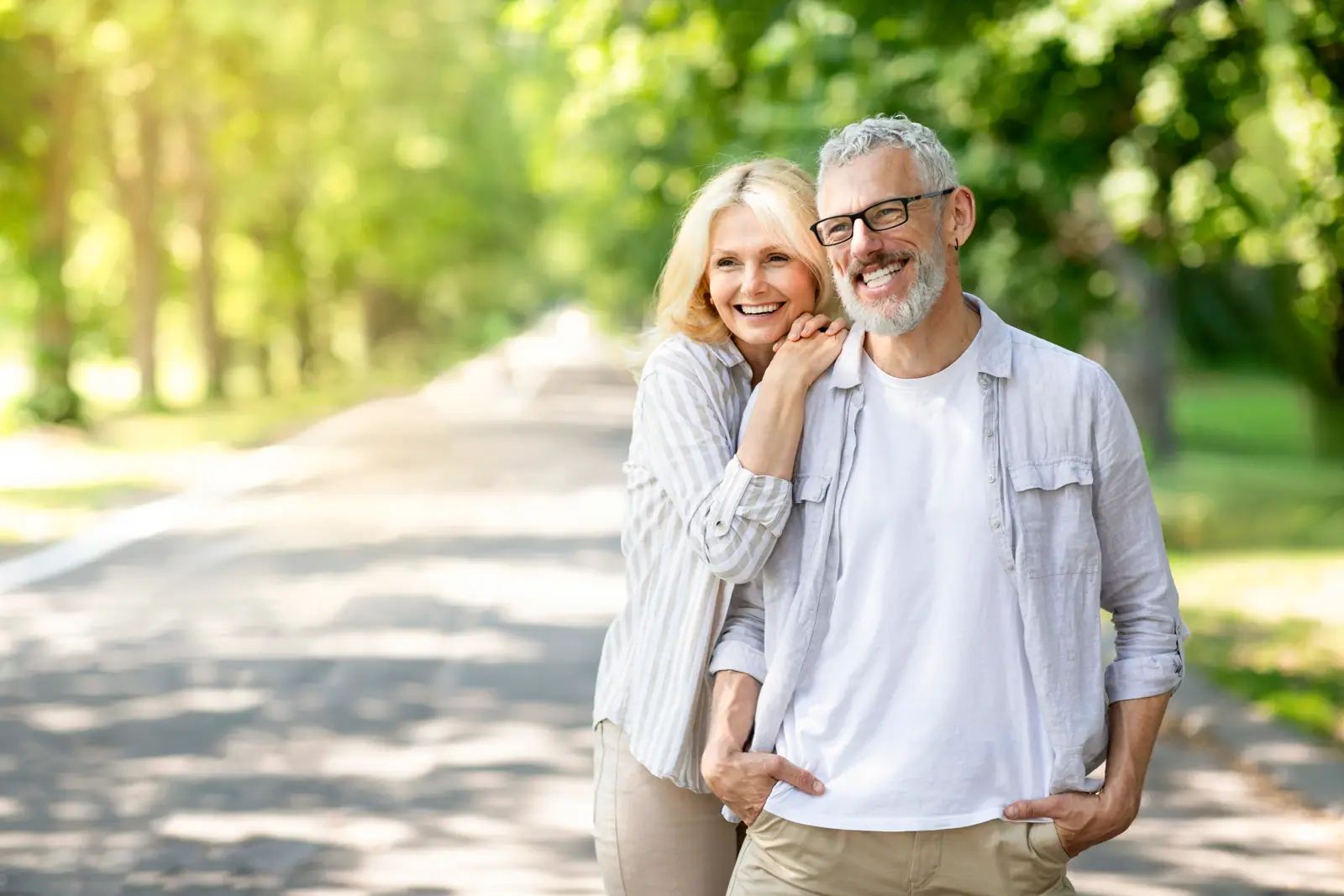 A smiling older couple on a sunny tree-lined path